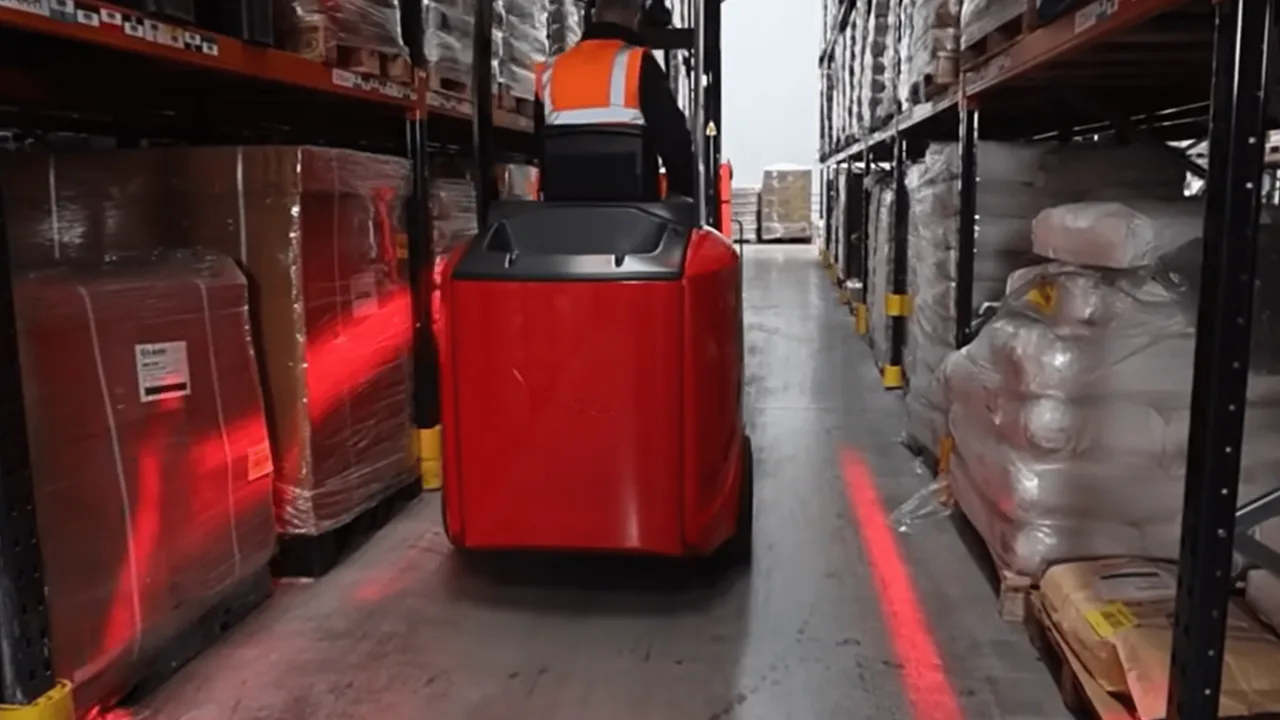 A red Flexi articulated narrow aisle forklift truck travelling down a guided very narrow aisle between tall pallet racking