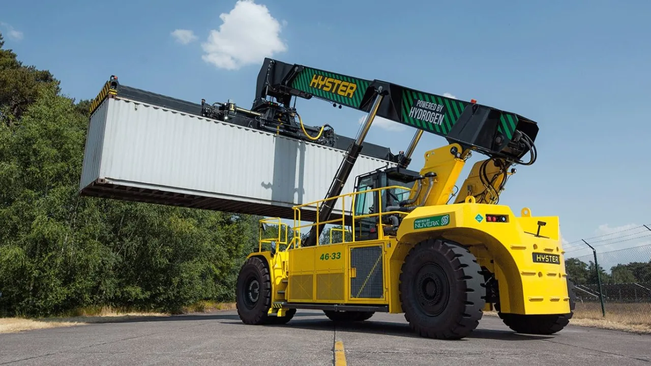 A yellow Hyster hydrogen powered reach stacker lifting a shipping container at a container terminal, with Hyster branding on the boom